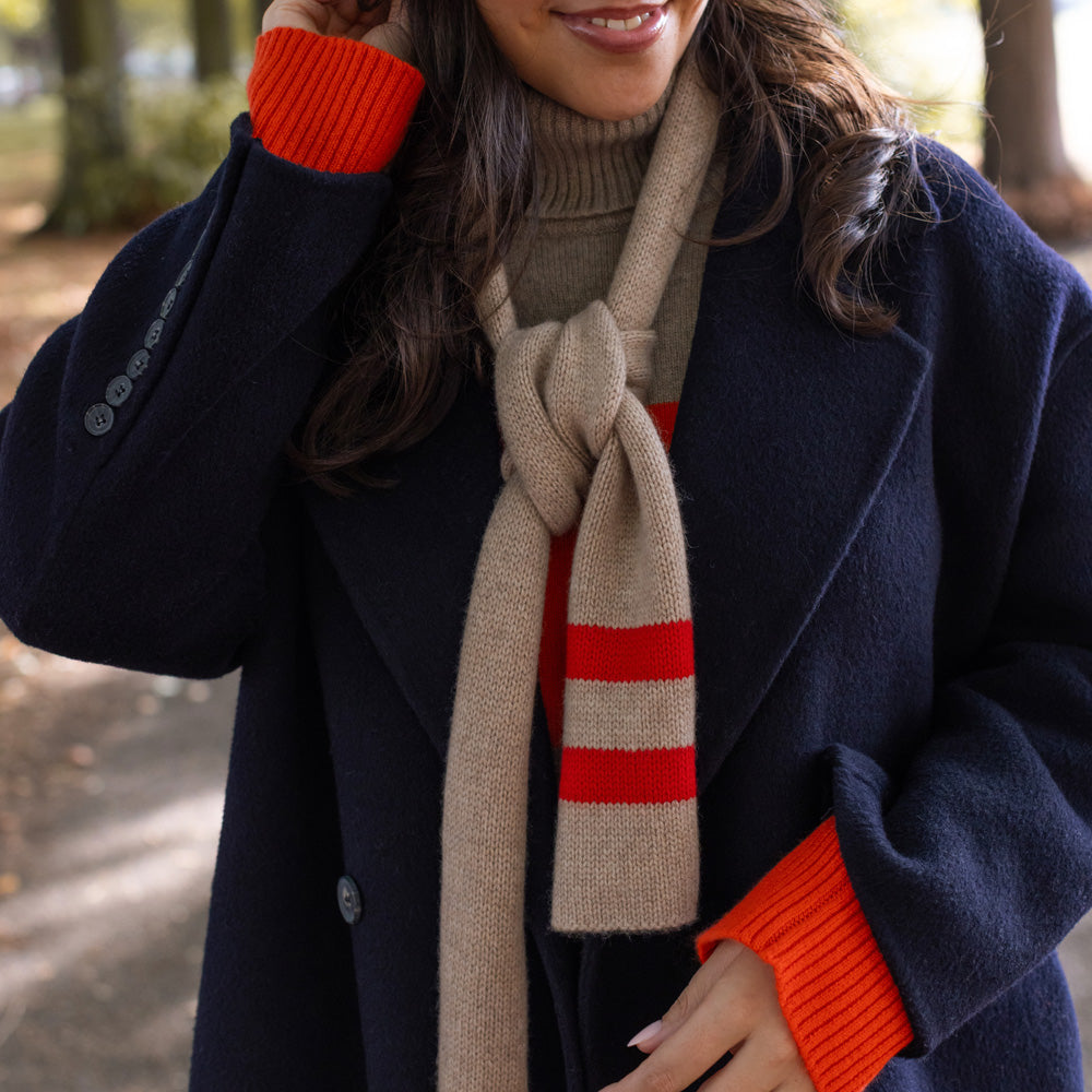 woman wearing a navy blue wool coat with a taupe and red jumper and a skinny taupe scarf with red stripes