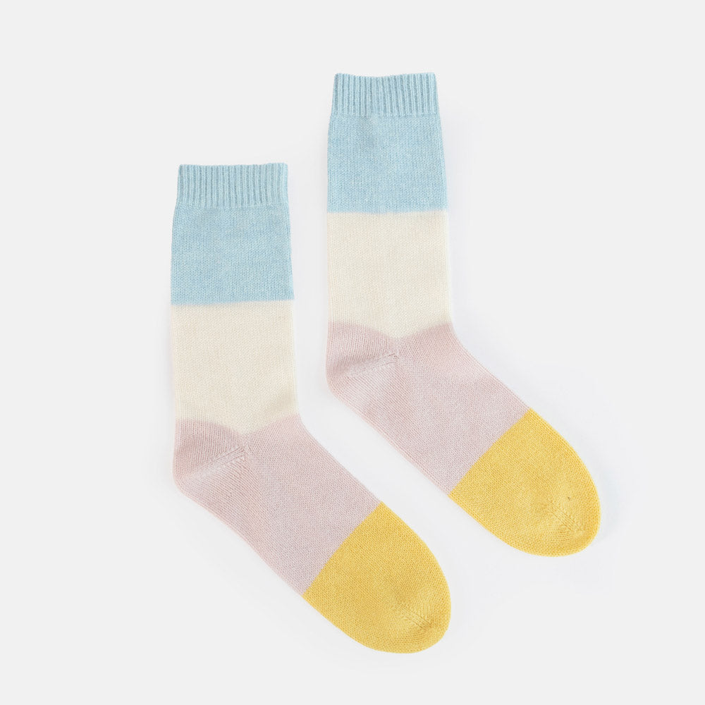 A pair of pastel color-block crew socks with a light blue ribbed cuff, cream upper section, pale pink lower leg, and yellow toes, displayed on a clean white background.