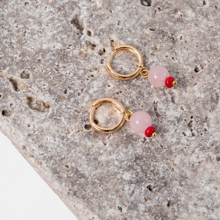 gold hoop earrings with pink semi precious stone and red glass bead on a marble surface