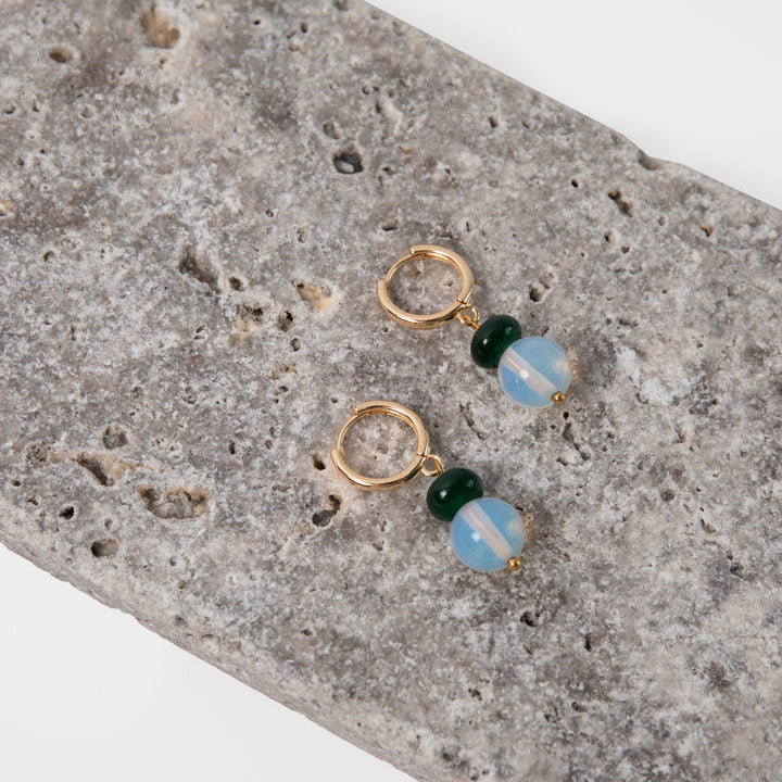 Pair of gold earrings with green and blue beads on a textured stone surface