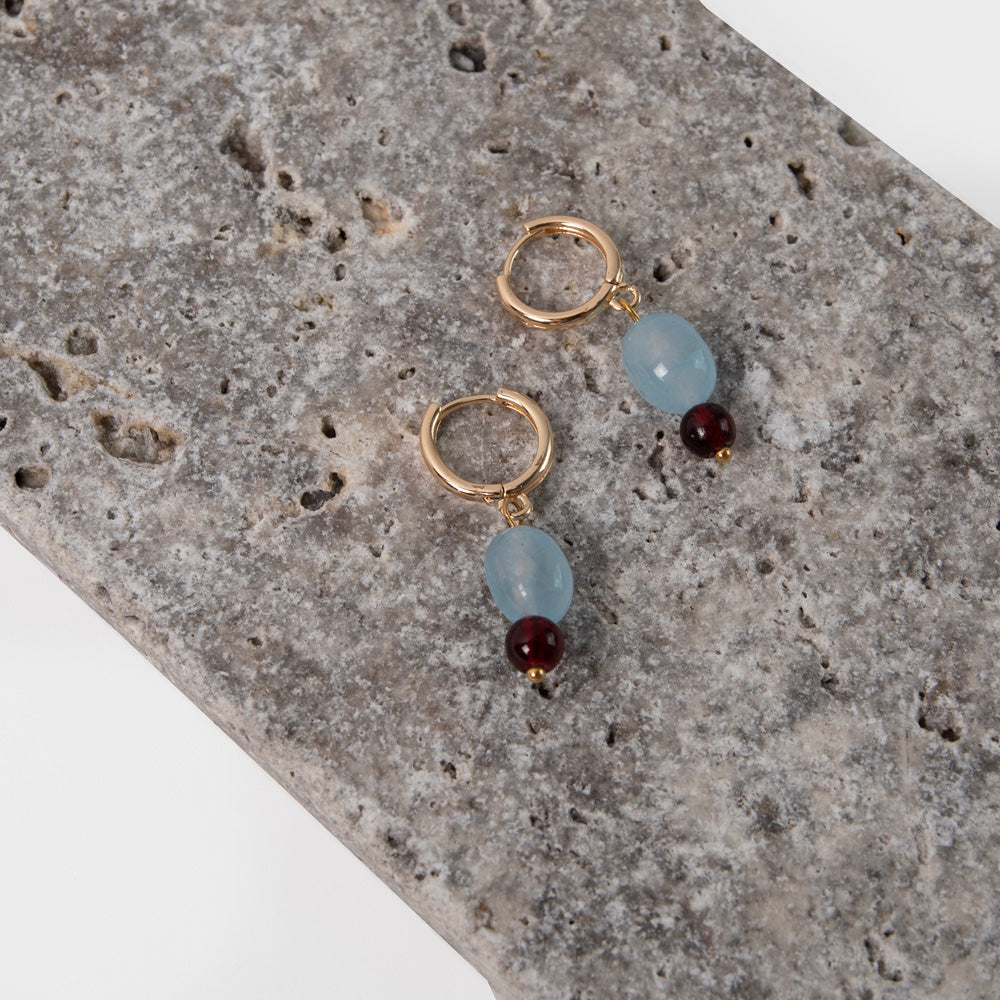 pair of gold hoop earrings with light blue and burgundy beads on a stone background