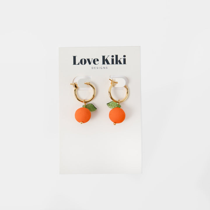 gold hoop earrings with orange shaped charms with green leaves in love kiki branded packaging