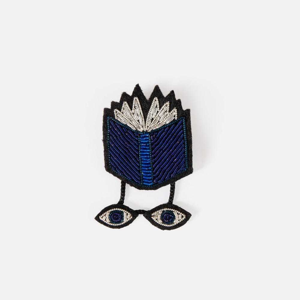 Blue book hand embroidered brooch with dangling eyes in a black presentation box.