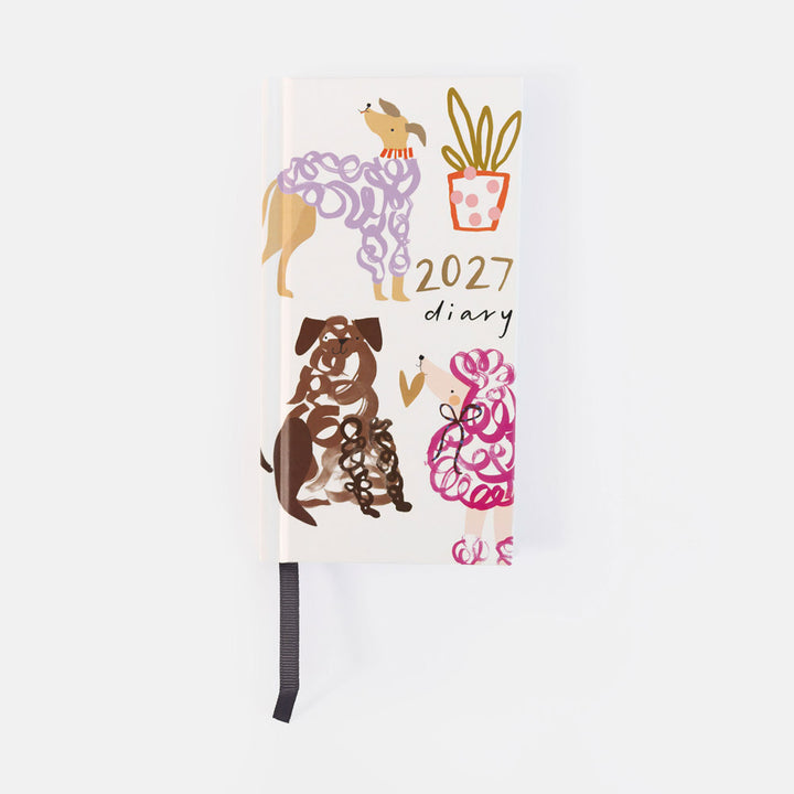 A 2027 daily planner with a white cover decorated with whimsical dog illustrations in purple, brown, and pink, along with a potted plant and gold text. A black ribbon bookmark hangs from the bottom.