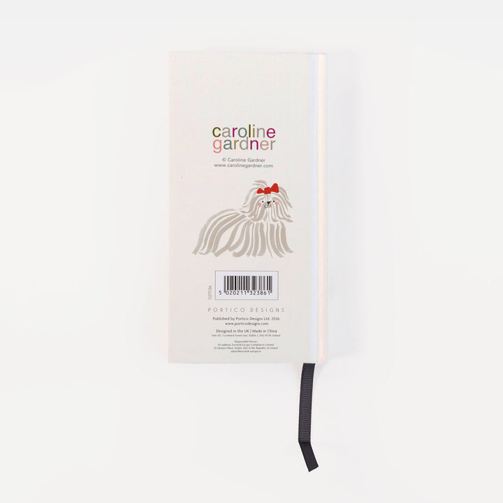 A slim notebook or journal with a white cover, featuring the text 'caroline gardner' and a line drawing of a long-haired dog with a red bow. A black ribbon bookmark hangs from the bottom edge against a plain white background.