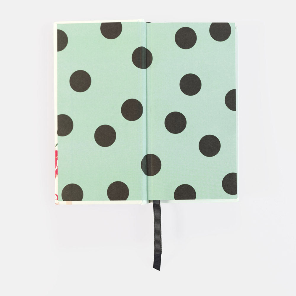 A notebook with a mint green cover decorated with large black polka dots, shown open against a plain white background with a black ribbon bookmark hanging from the center.