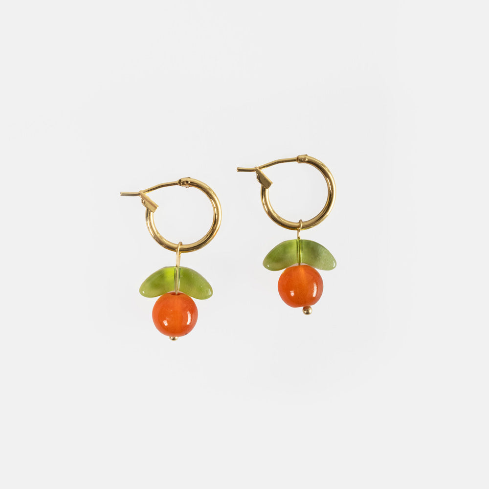 A pair of gold hoop earrings each with a glossy orange glass bead and a green glass leaf, like a little clementine, on a light grey background.