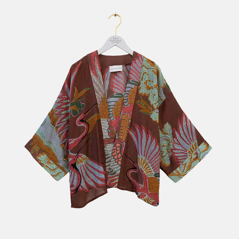 A brown open-front kimono-style top with wide three-quarter sleeves, featuring a detailed botanical and bird pattern in green, blue, and pink. The garment is displayed on a white hanger against a light gray background.