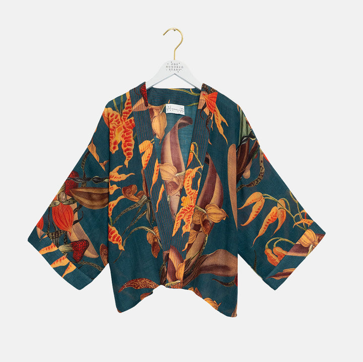 A short-sleeved kimono-style top with wide sleeves, featuring a botanical print of orange, red, and brown flowers on a dark teal background. The top is displayed on a white hanger with a gold hook against a light gray background.