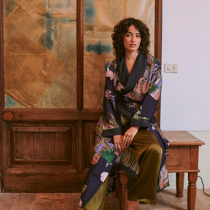 A woman wearing a long-sleeved wrap robe with a black shawl collar and waist tie, featuring a highly detailed, multicolored botanical and animal print
