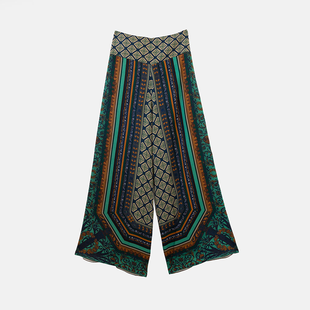 A pair of wide-leg palazzo pants featuring a complex geometric and tribal-inspired pattern in teal, navy, brown, and beige, displayed against a light gray background.