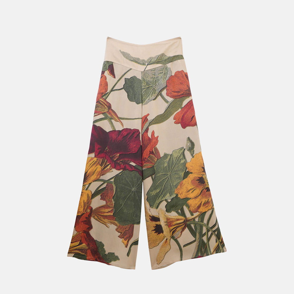 A pair of wide-leg cropped pants featuring a vintage botanical floral print on a beige background with red, yellow, and orange flowers and green leaves, shown against a light gray studio background.