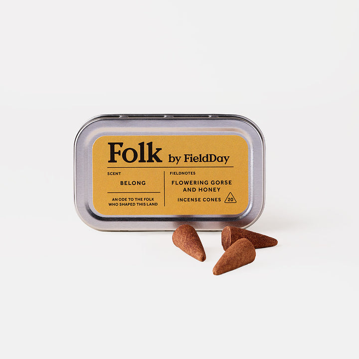 A silver metal tin of Folk by FieldDay incense cones with a mustard yellow label, shown on a clean white background with three brown incense cones placed in front.