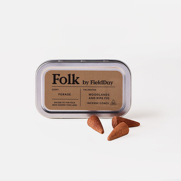A silver metal tin of Folk by FieldDay incense cones on a white background, with three brown incense cones placed in front of the tin.