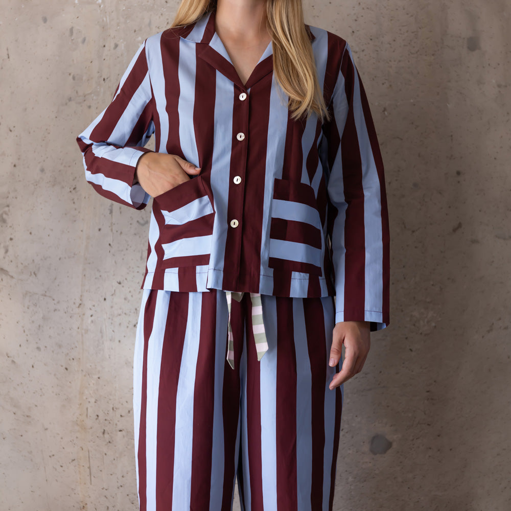 Woman wearing a blue and wine wide-stripe pyjama set, one hand in the shirt's front pocket
