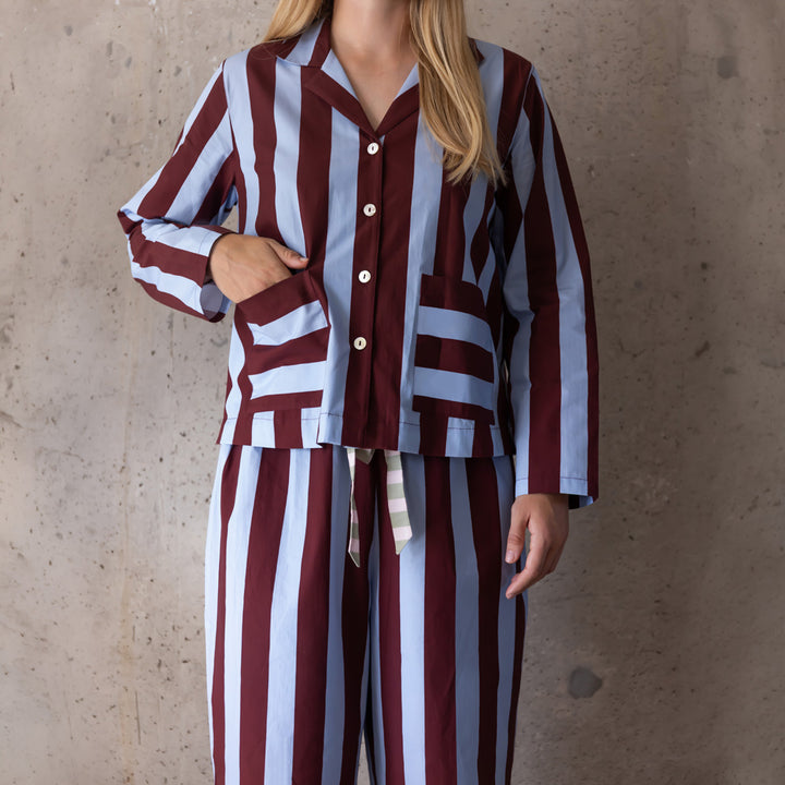 Woman wearing a blue and wine wide-stripe pyjama set, one hand in the shirt's front pocket