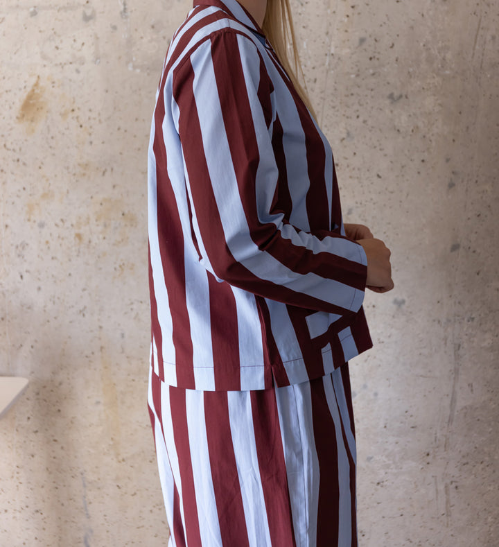 Side view of a woman wearing a long-sleeved blue and wine striped pyjama shirt