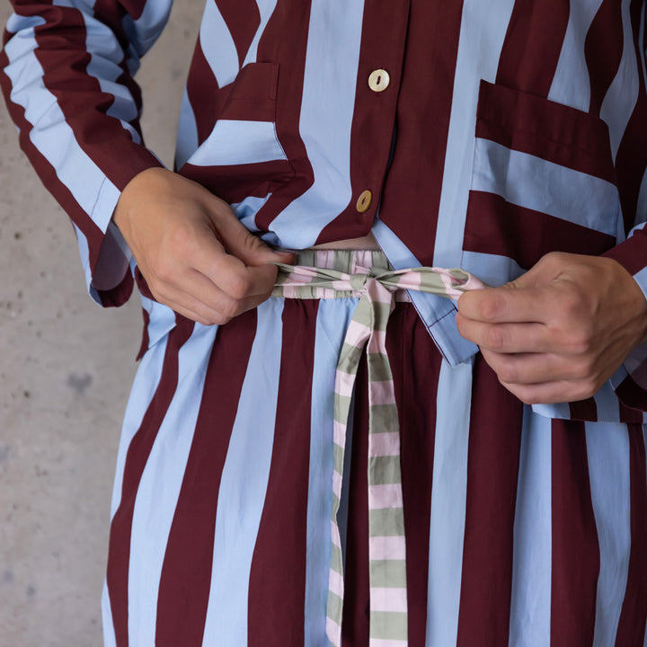 Close-up of hands tying a pink, green and cream striped cord at the waist of striped pyjama trousers