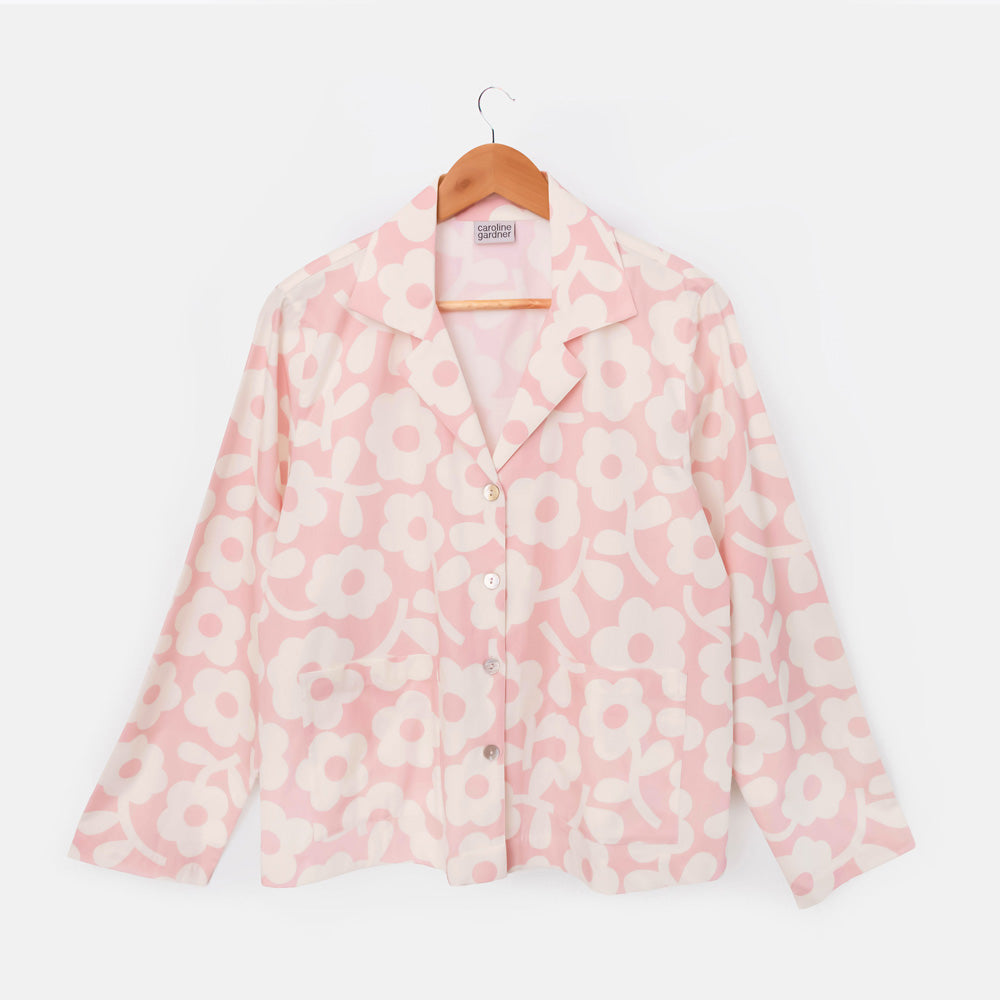 Long-sleeved pale pink pyjama shirt with a revere collar and bold cream flower print on a hanger