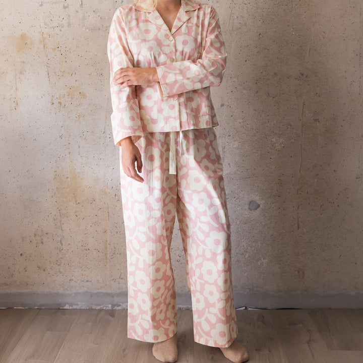 Woman wearing a pale pink and cream flower print long pyjama set with wide-leg trousers