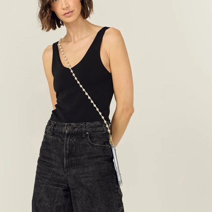 Woman in a black vest wearing a pearl phone chain crossbody with jeans