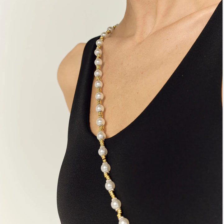 Close-up of a pearl and gold chain worn across the shoulder over a black top