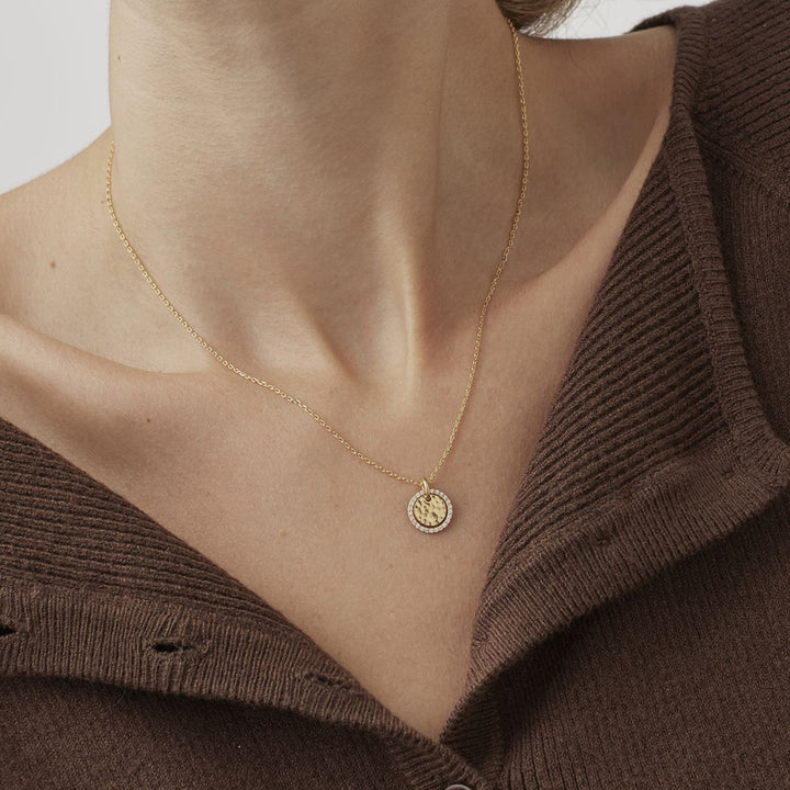 Woman wearing a gold chain with a small coin pendant over a brown knit