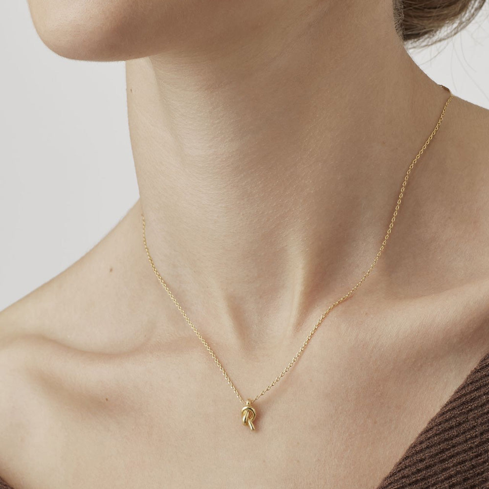 Woman wearing a fine gold necklace with a knot pendant