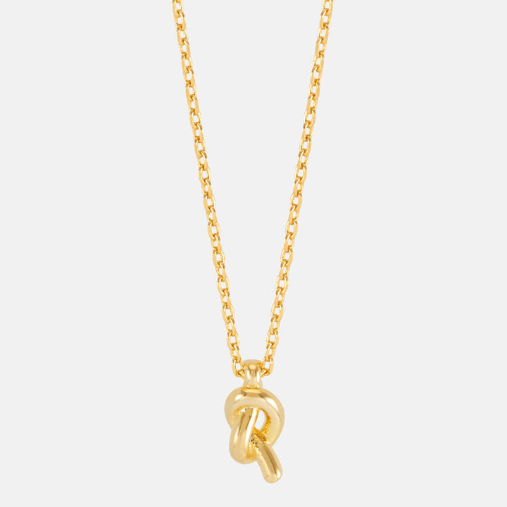 Close-up of a polished gold knot pendant on a chain