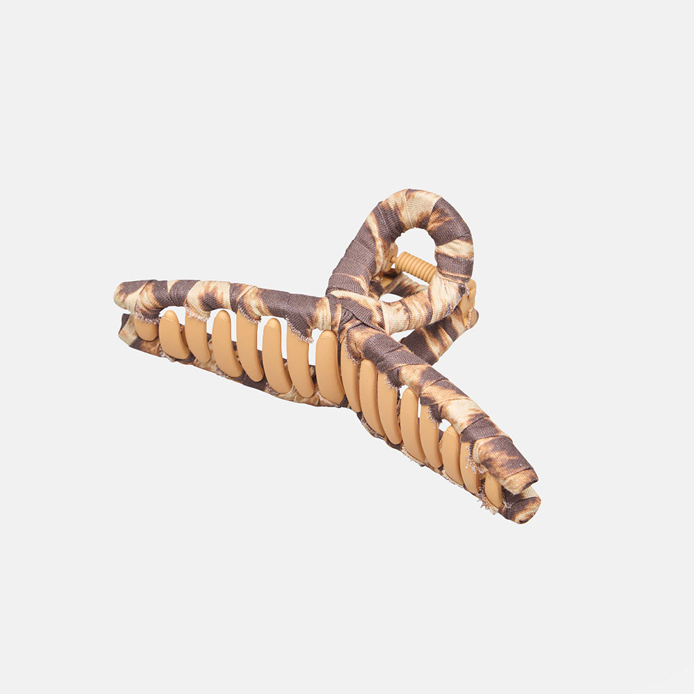 A large hair claw wrapped in printed fabric in sand, caramel and brown tones, on a light grey background.