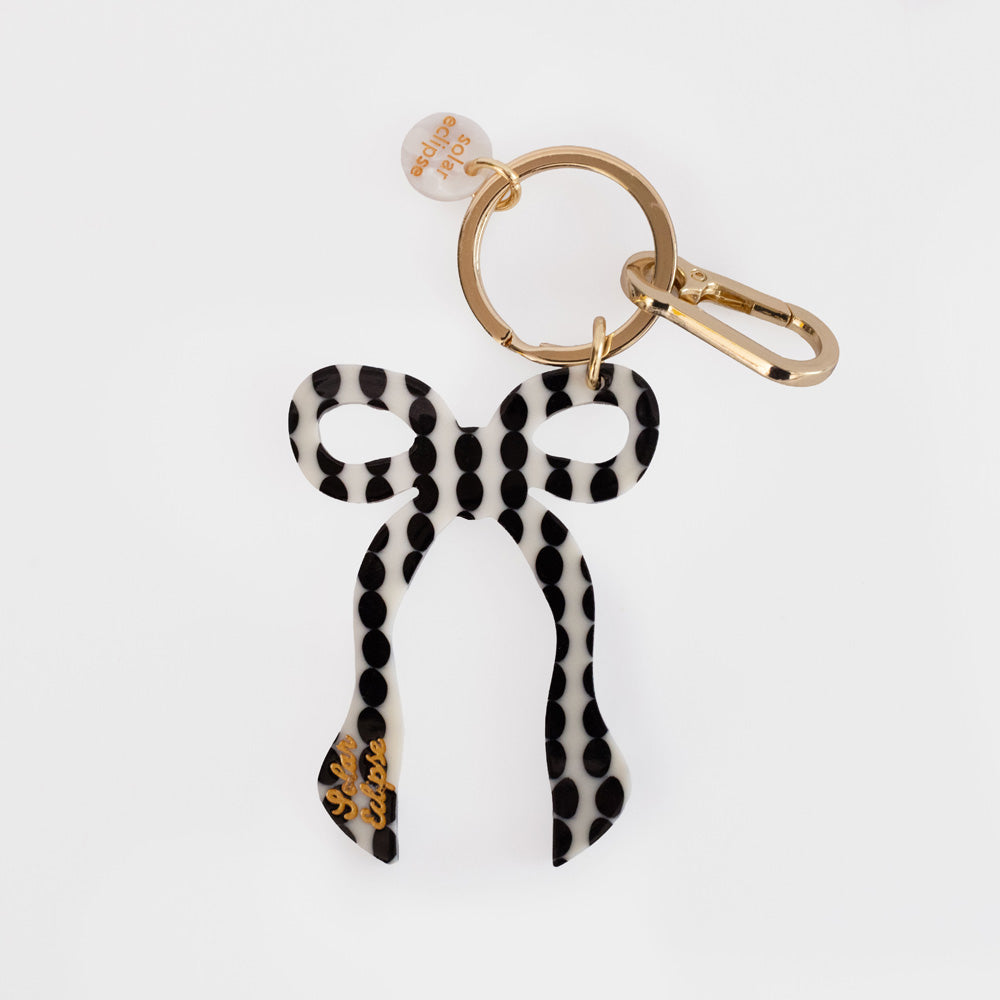 Black and cream dotted bow-shaped charm on a gold key ring with a gold clip