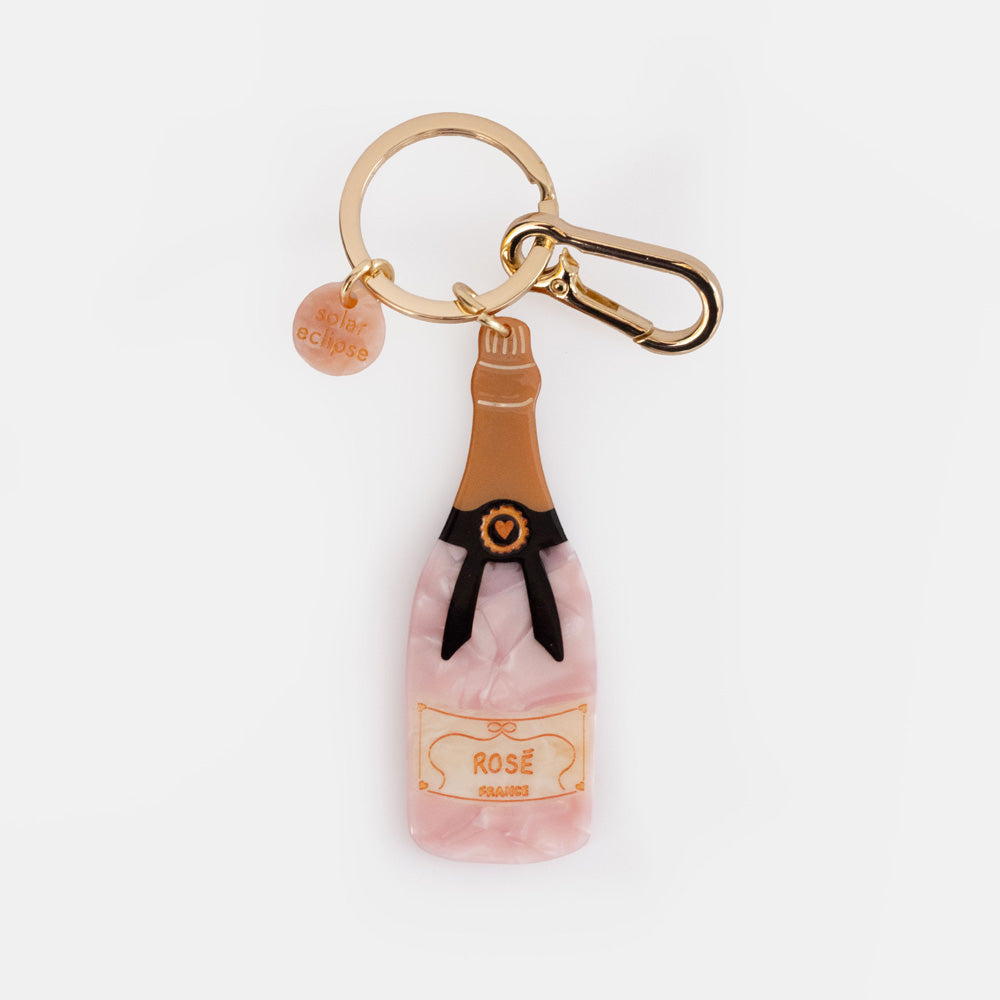 Pink marbled champagne bottle charm with a copper top, black ribbon and Rosé label on a gold key ring and clip