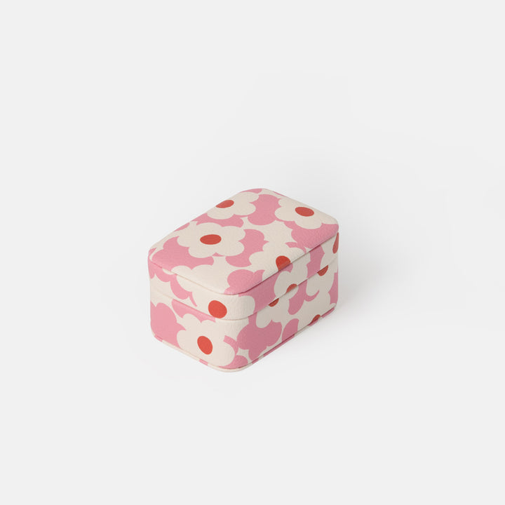 A small rectangular jewellery box with rounded corners, featuring a pink and off-white floral pattern with red centers, set against a plain light gray background.