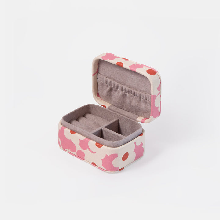 An open rectangular jewelry box with a pink and red abstract pattern on a cream exterior and a gray velvet interior, shown on a light gray background.