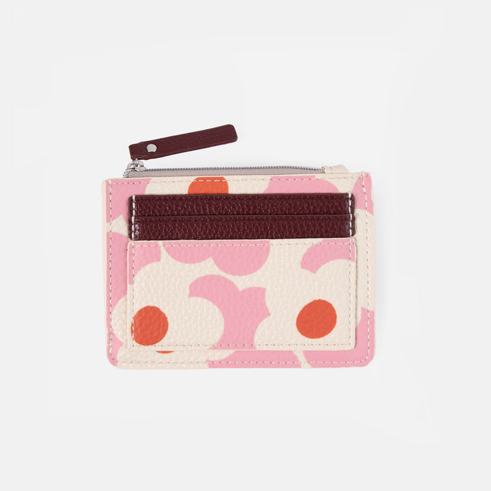 A small card holder or wallet with a pink and cream floral pattern, a dark brown textured horizontal band, and a dark brown zipper pull, shown on a light gray background.