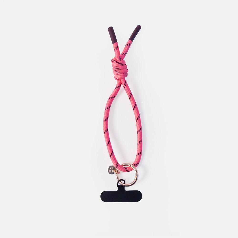 A pink braided cord phone strap with a knot, a small gold ring, and a black plastic clip, shown on a light gray background.