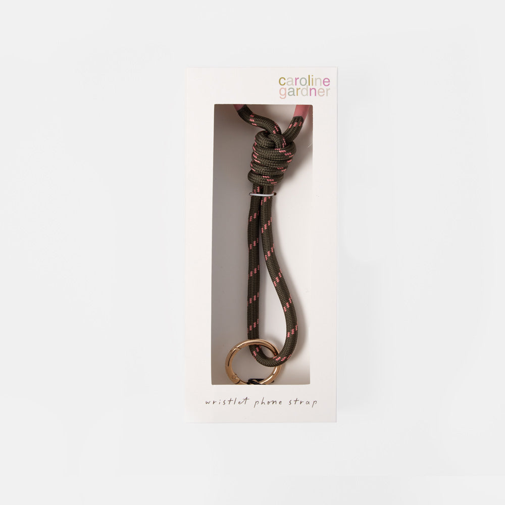 Caroline Gardner wristlet phone strap in a black and pink paracord pattern with a gold metal ring, shown inside its white retail packaging.