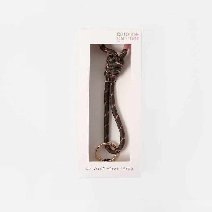 Caroline Gardner wristlet phone strap in a black and pink paracord pattern with a gold metal ring, shown inside its white retail packaging.
