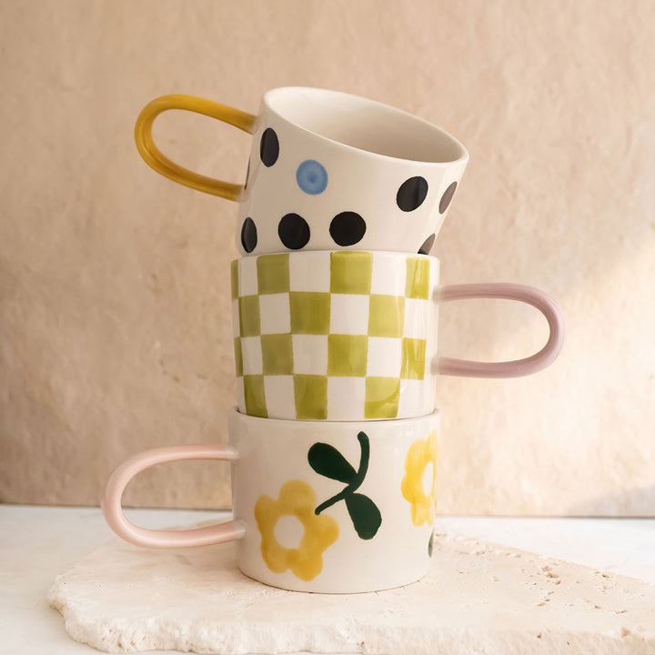 STACK OF 3 MUGS IN YELLOW FLORAL DESIGN, GREEN GRID CEHCK DESIGN AND BLACK AND BLUE SPOT DESIGN