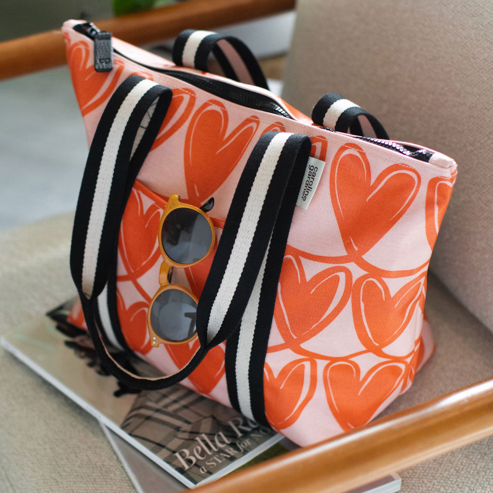 a pink and red tote bag with looped hearts design and black and white webbing straps on a chair