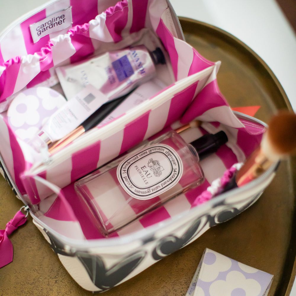 flat lay washbag with pink striped lining and toiletries inside in compartments