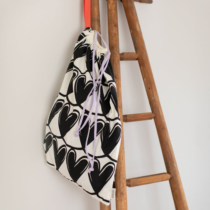 Drawstring laundry bag with black heart pattern hung on a wooden ladder
