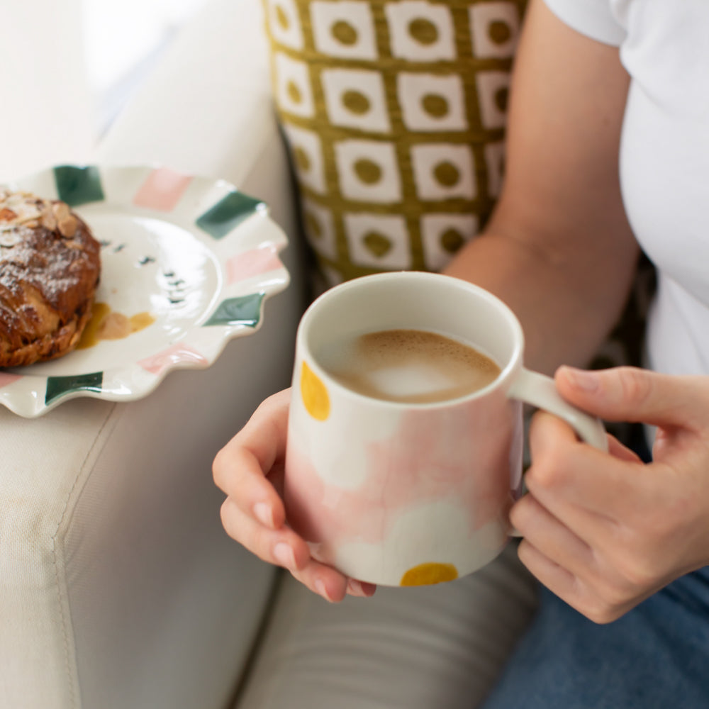 person holding a large pink ceramic mug with white & yellow flower design