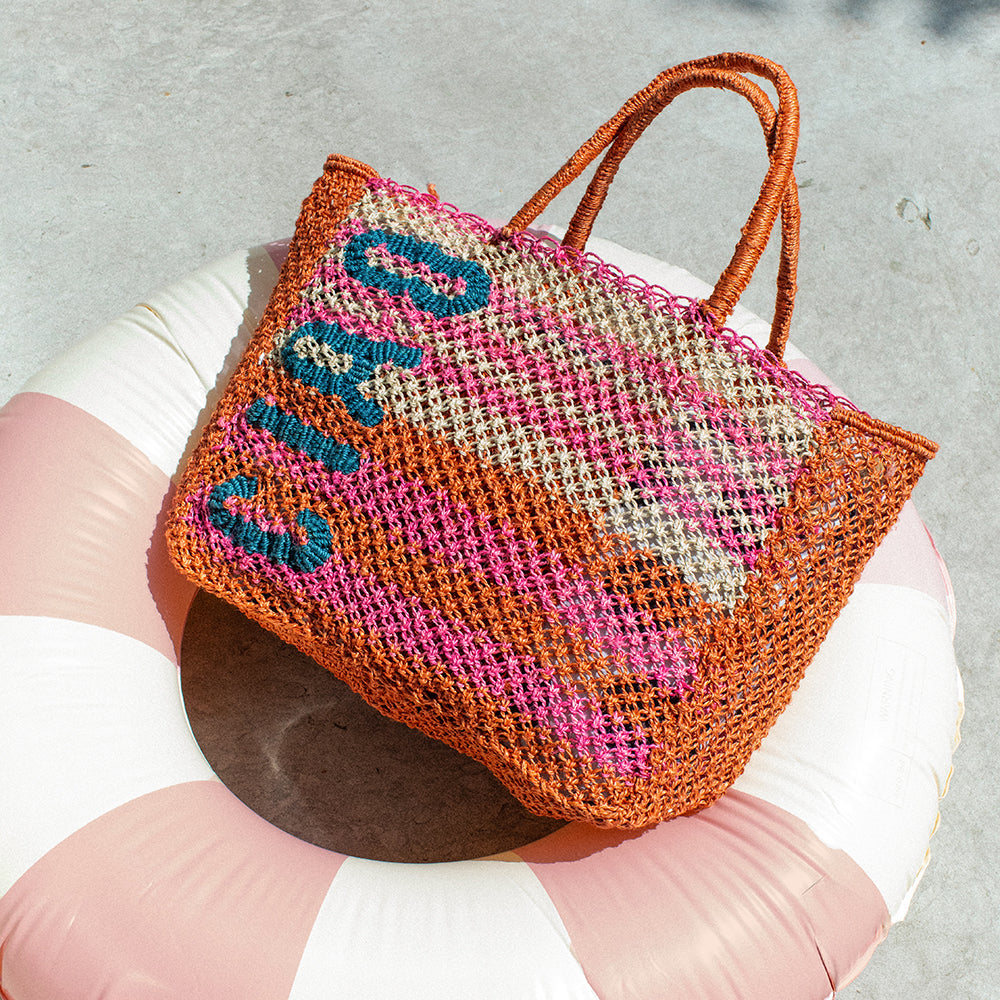 Woven bag with 'Ciao' text on a white and pink inflatable ring against a gray background