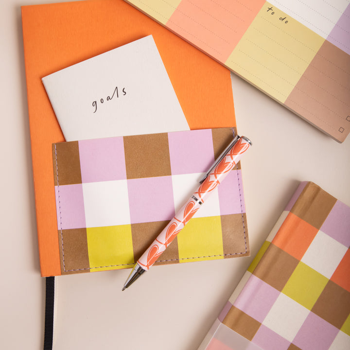 assorted colourful stationery with a red & pink hearts print pen, and multicoloured checked notebooks