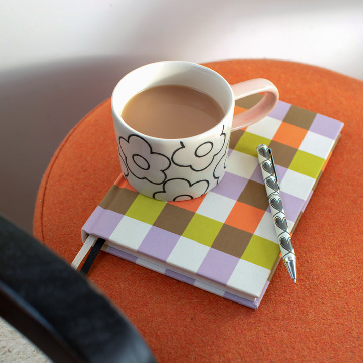 flower print mug sat on top of a colourful checked notebook with a back & white heart print pen