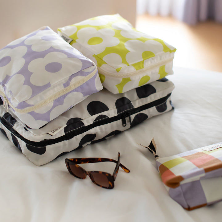 set of 3 packing cubes in colourful flower designs on a white bed with a pair of sunglasses