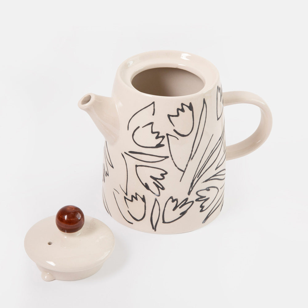 A cream-colored ceramic teapot with a black line-art floral pattern, shown with its matching lid on a clean white background.