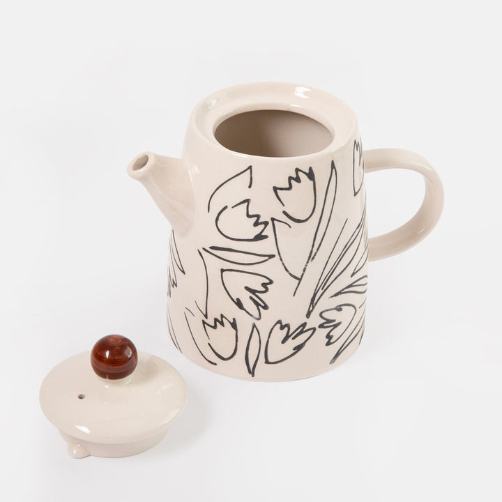 A cream-colored ceramic teapot with a black line-art floral pattern, shown with its matching lid on a clean white background.