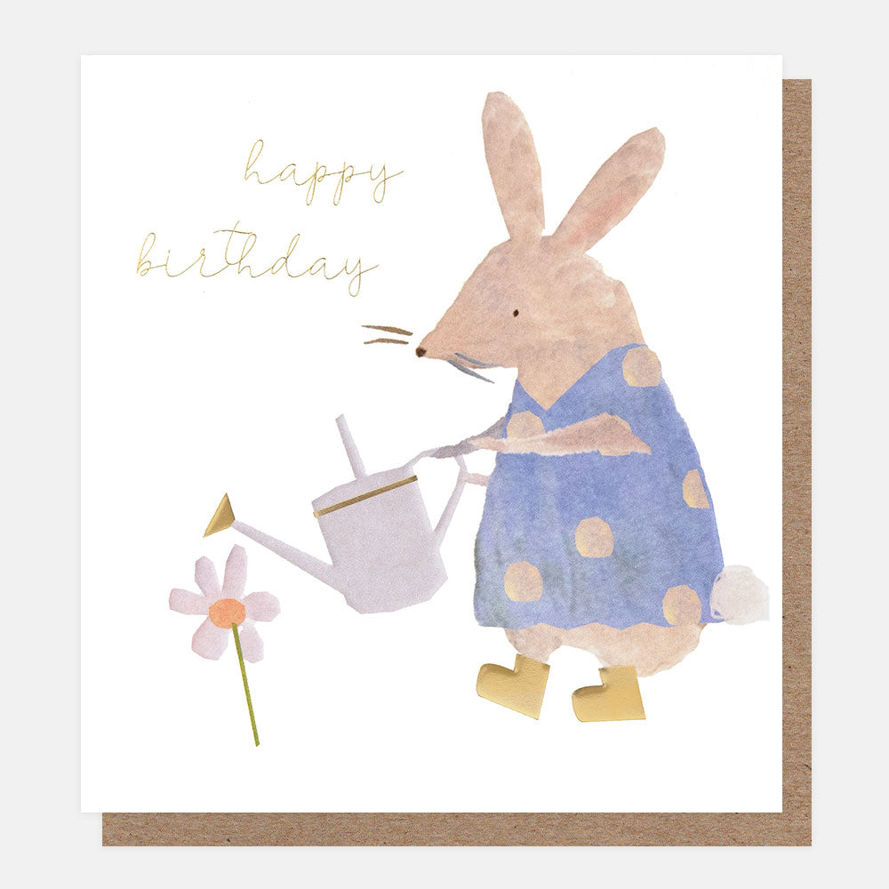 birthday card featuring a rabbit dressed in a blue spotty top and gold wellington boots watering a small daisy flower with a watering can, and the text happy birthday 